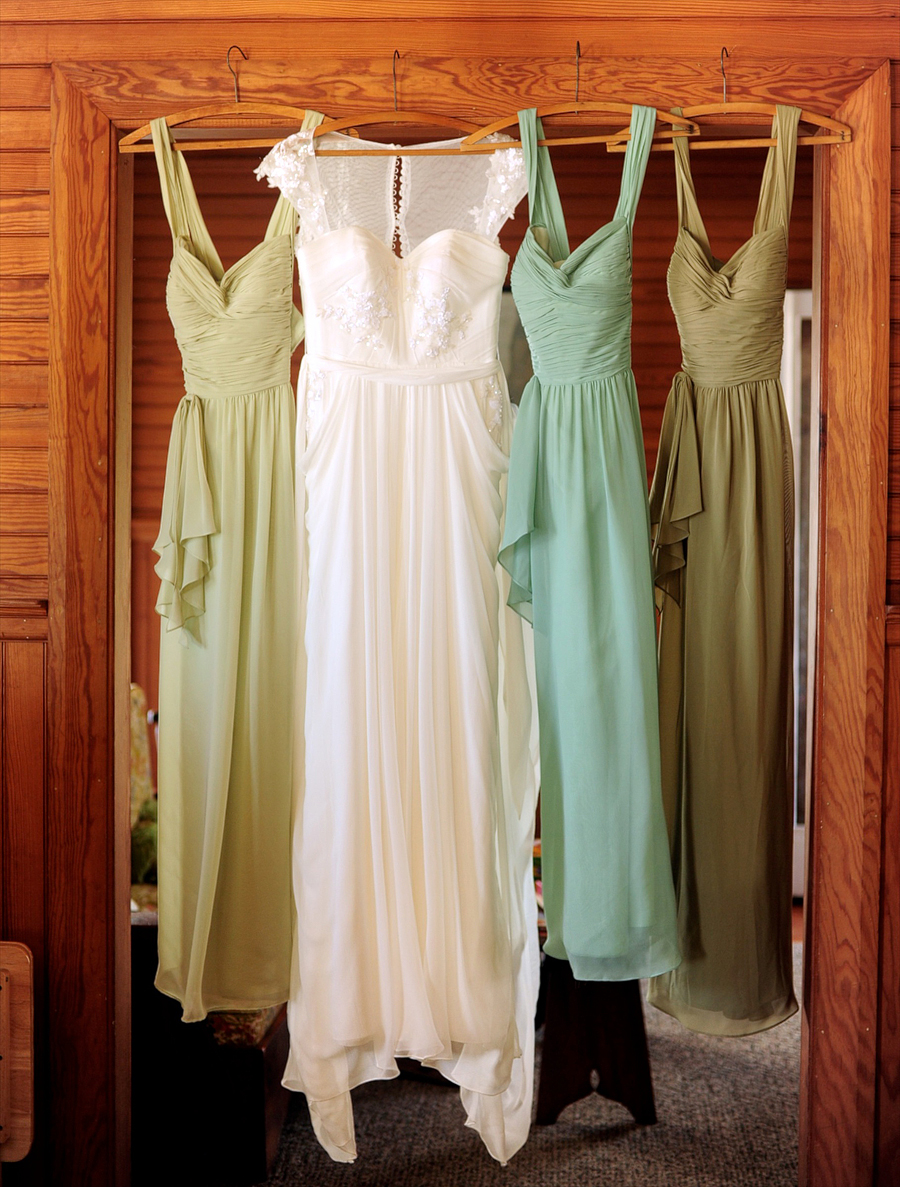 bride's dress hanging with green bridesmaid dresses