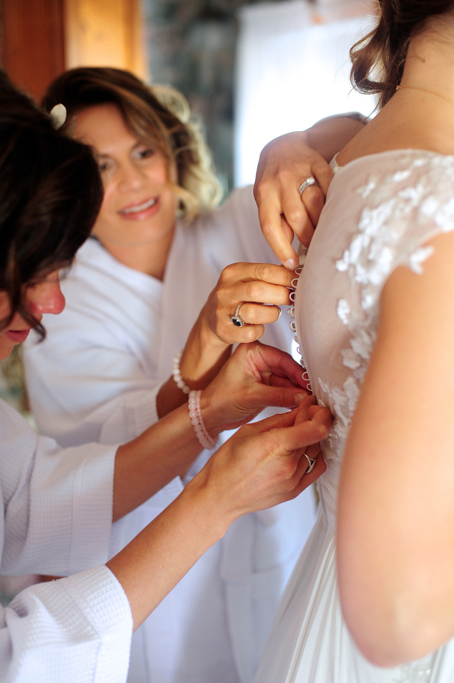 bridesmaid buttoning up bride's wedding dress