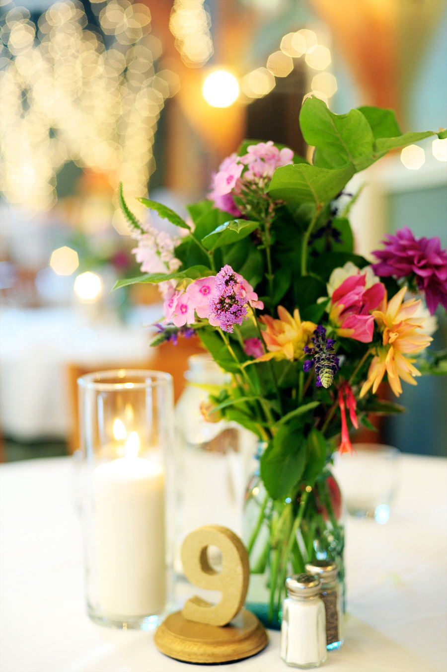 colorful wildflower centerpiece with a gold table number and twinkling lights