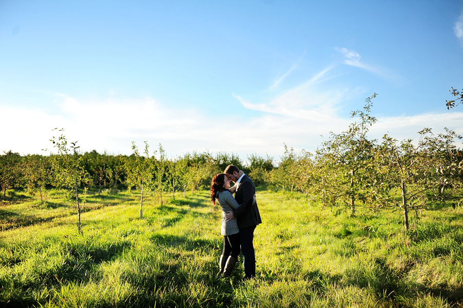 couple snuggling in an open field with a blue sky