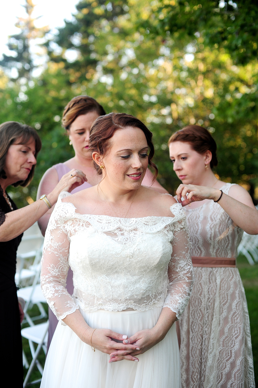a bride being helped by her mom and sisters with her lace bolero