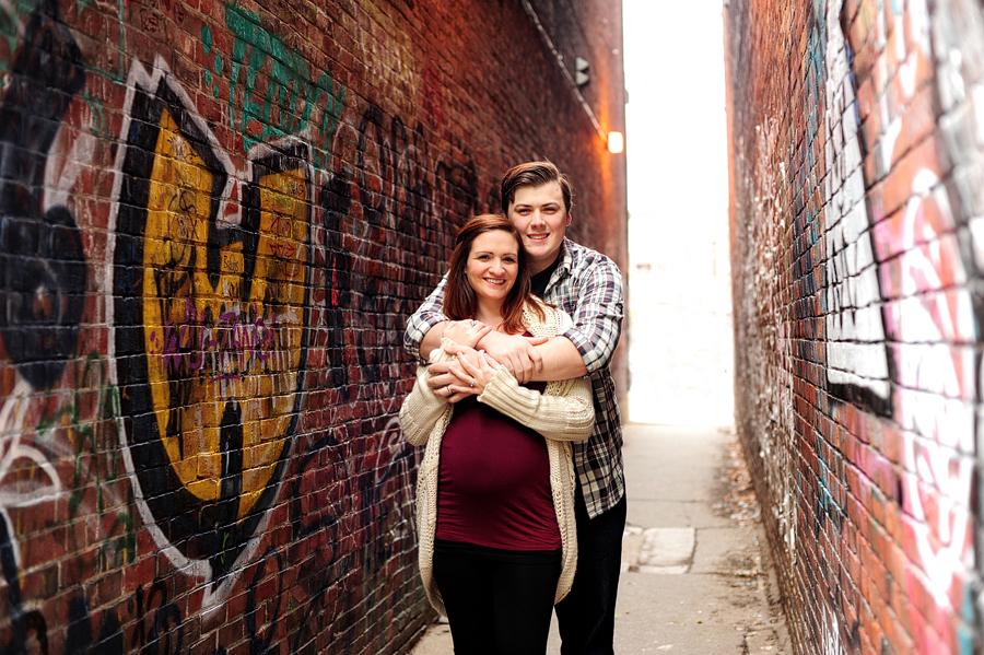 smiling pregnant couple in alleyway