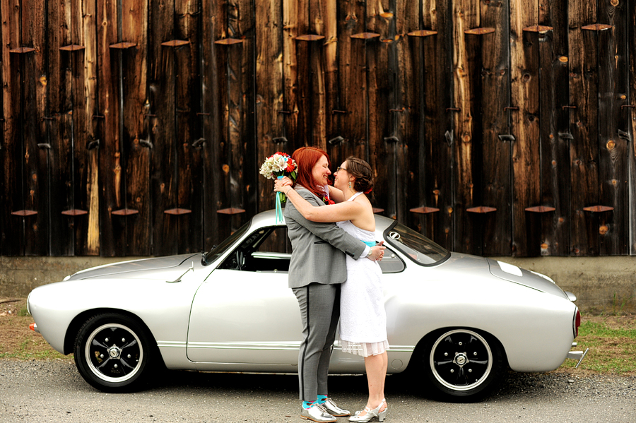 brides posing in front of silver sports car