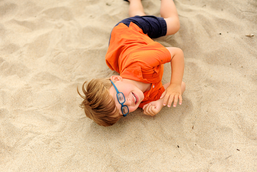 kid rolling in sand at the beach