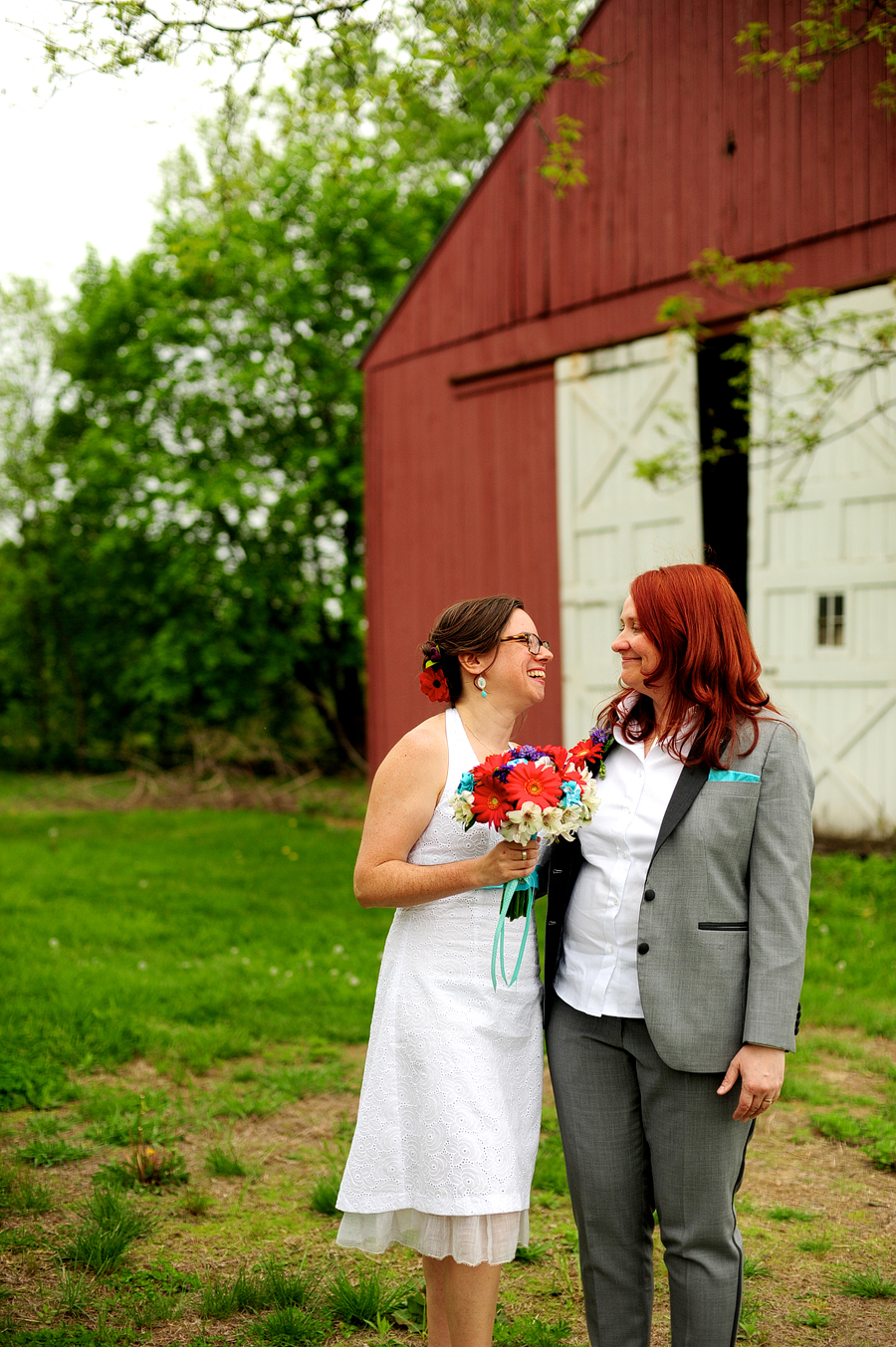 brides posing near a red barn