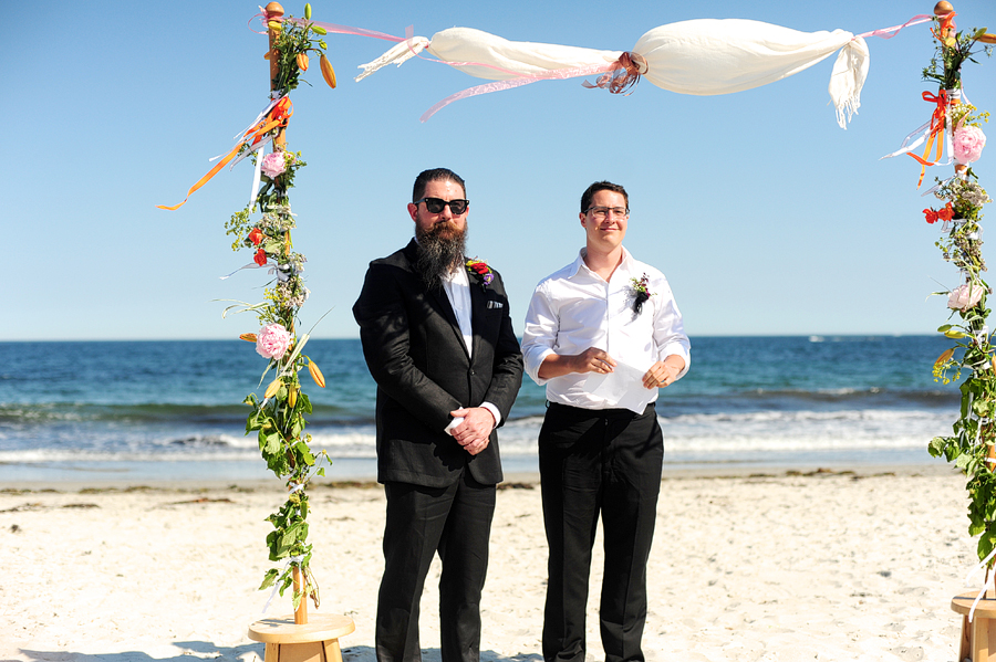 groom waiting at floral arbor on crescent beach