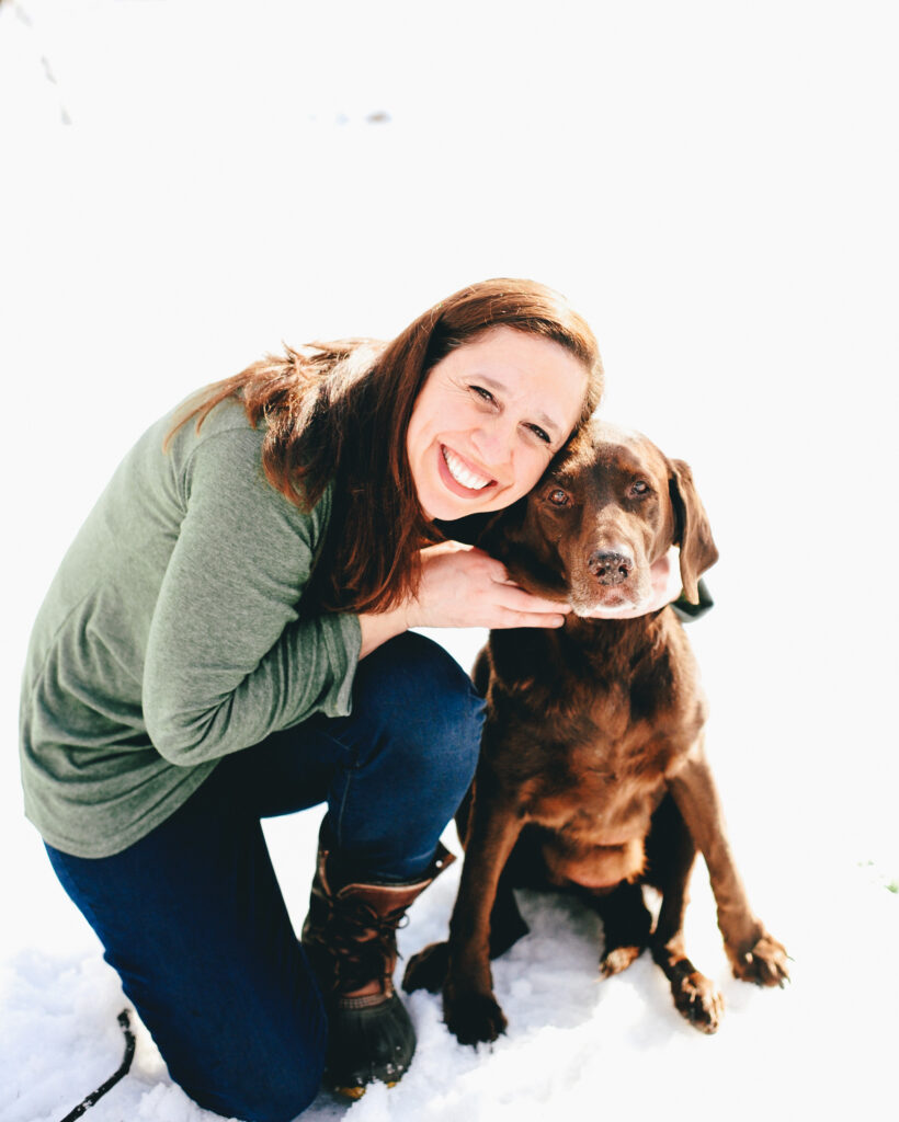 a smiling woman hugs her brown dog