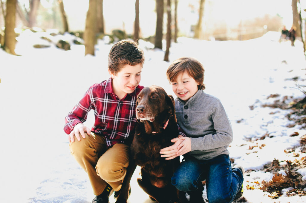 two brothers smile at their brown dog