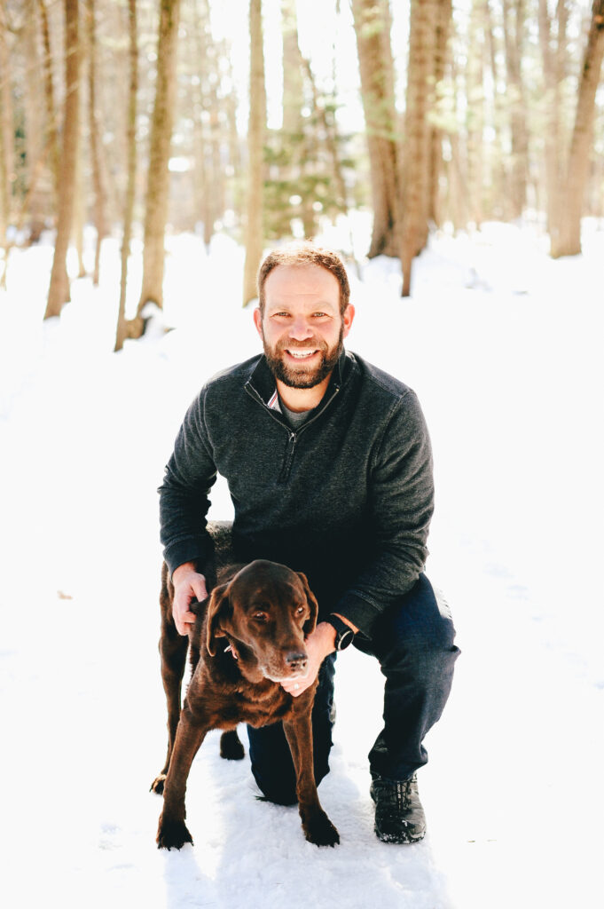 a man posing in the snow with his brown dog