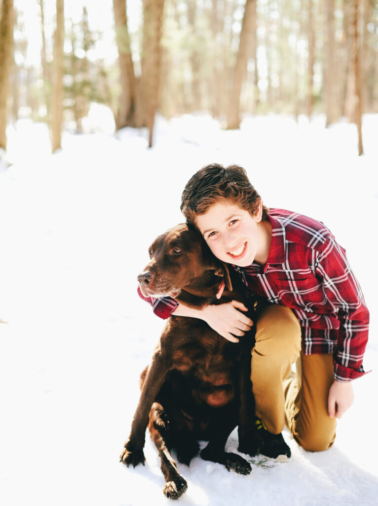 a young boy in a plaid shirt hugs his dog